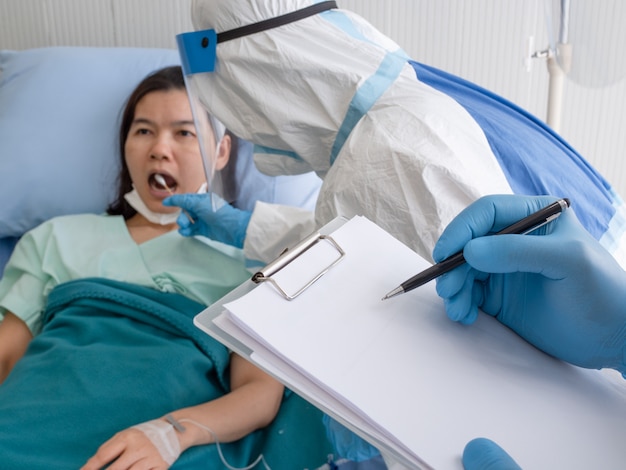 Photo two asian doctor wear ppe with mask and face shield, using cotton swab to do buccal swab sample collection for coronavirus testing from patient in quarantine room.