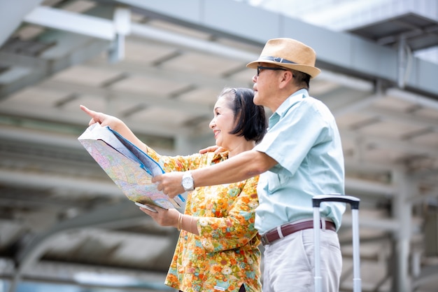 two Asian elderly travelling with map and luggage against building  