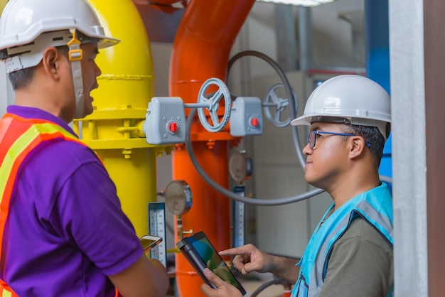 Два азиатских инженера, работающие в котельной, проверяют технические данные оборудования системы отопления. Жители Таиланда обсуждают вопрос о давлении в трубе.