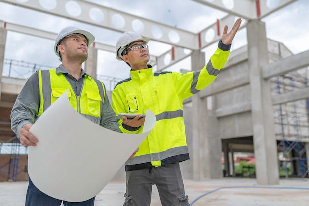 Two Asian engineer working at site of a large building projectWork overtime at construction siteTeam of engineer discus at siteThe architect supervisor and foreman meet to discuss the design