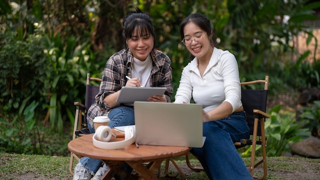 Two Asian female are talking and working on a project together while sitting at an outdoor table