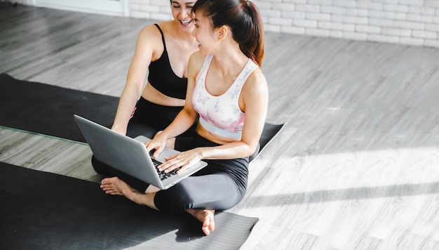 Foto due donne asiatiche in una suite di yoga che utilizzano un computer portatile che praticano online, concetto di stile di vita sano della donna, spazio di copia