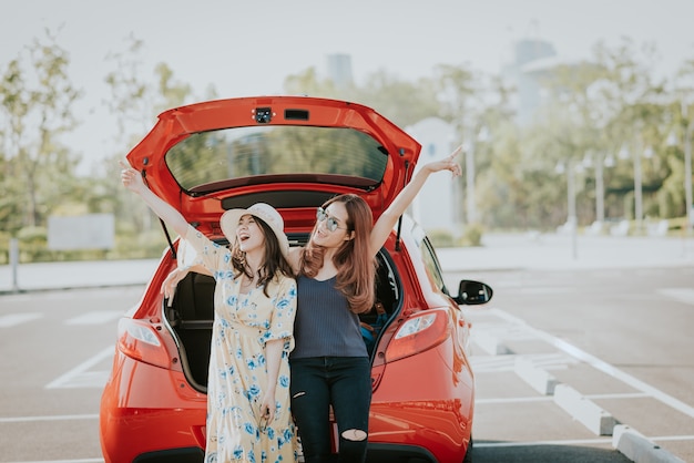 Two Asian girl best friends celebrating a good time while sitting in car trunk 