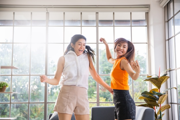 Two asian girl friends dancing in living room at home