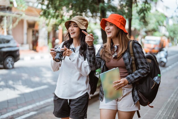 Photo two asian girls backpacking to find tourist destinations with cameras and maps on the side of the