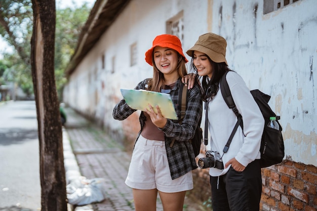 두 명의 아시아 소녀는 관광지로 가는 길을 찾기 위해 지도를 보고 있습니다.