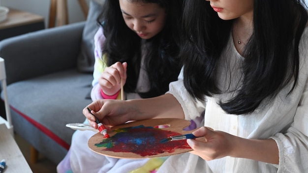 Two asian girls spending leisure time together at home and painting picture with water color