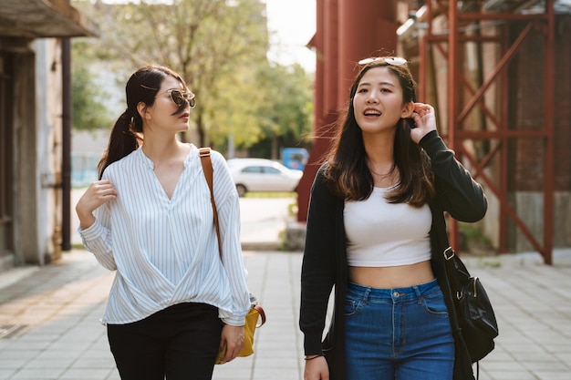 Two asian japanese female friends relax walking outdoors together in red old factory. group of young beautiful girls tourists sightseeing in historic tourism attraction on sunny day in summer time.