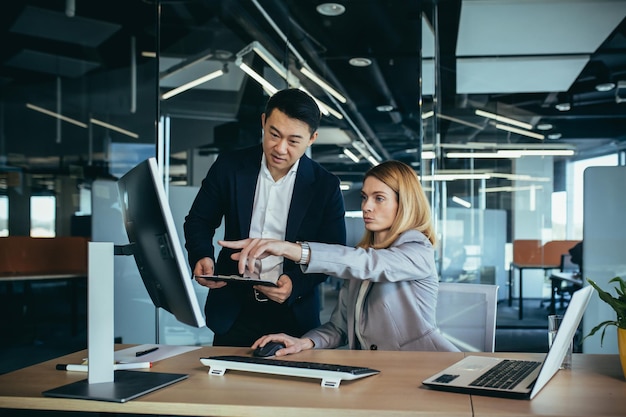 Due colleghi asiatici maschi e femmine in un ufficio moderno una donna mostra il lavoro svolto sul monitor consulta e discute