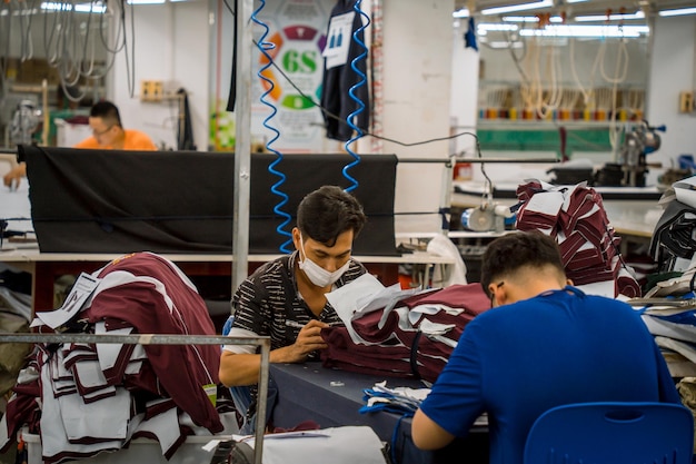 Two asian man wearing medical mask writing number on fabric after finished cut Textile cloth factory working process tailoring workers equipment