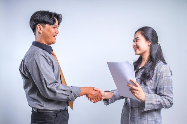 Photo two asian man and woman wear formal clothes standing face to face and handshaking while holding pape