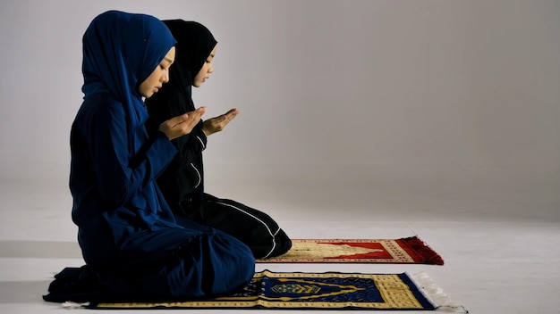 Two Asian Muslim young women in traditional hijab are praying glorify Allah and practicing the Islamic faith in mosque
