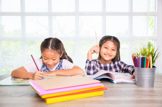 2人のアジア人学生の女の子が家で昼間に本を書いて学んで楽しむ