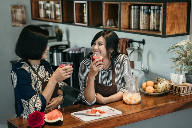 2つのアジアの女性はキッチンで甘い飲み物を楽しむ