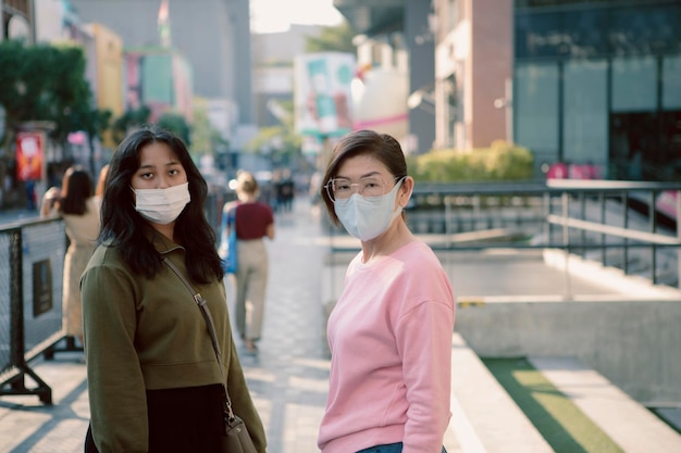 two asian woman wearing protection mask standing on bangkok city street