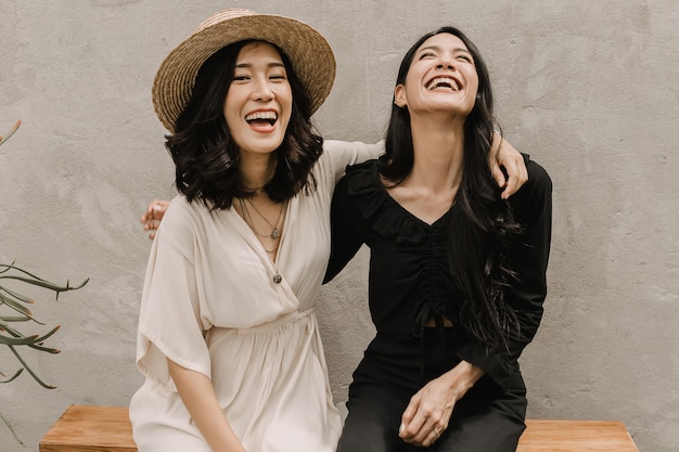 Two Asian women are hugging together while they are laughing and smiling