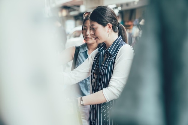 Two asian women choosing clothes in store searching buying\
cheap shirt on rack hanger at flea market stall shopping apparel\
fashion concept. young girl friends talking discuss dress outdoor\
vendor