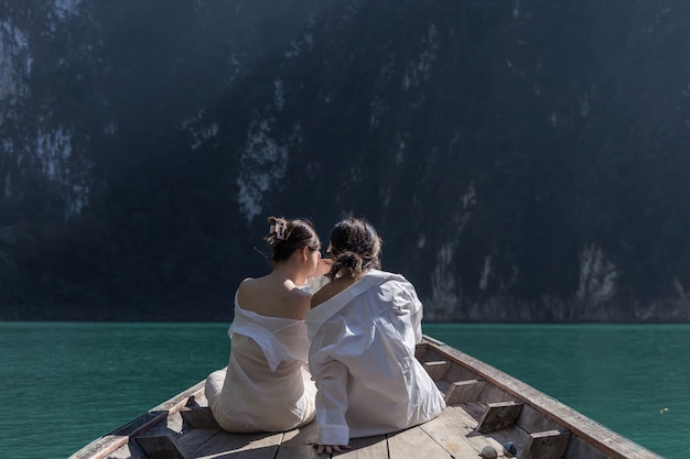 Due donne asiatiche in camicia bianca siedono davanti a una barca con una bellissima montagna in mezzo al mare durante un viaggio in thailandia. incredibile thailandia.