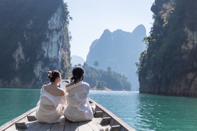 Due donne asiatiche in camicia bianca siedono davanti a una barca con una bellissima montagna in mezzo al mare durante un viaggio in thailandia. incredibile thailandia.