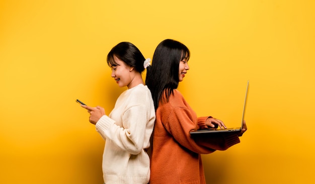 Two Asian women working on laptop and phone at the same time Two of them were communicating online and showing happy smiles