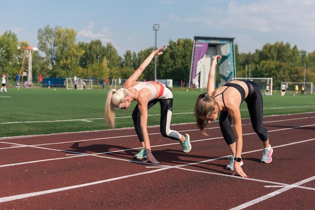 Due corridori della giovane donna dell'atleta all'inizio allo stadio all'aperto