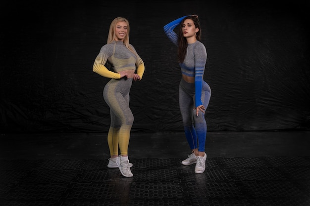 Фото Две спортивные девушки с уверенным взглядом позируют на темном фоне, одетые в яркую одежду для фитнеса