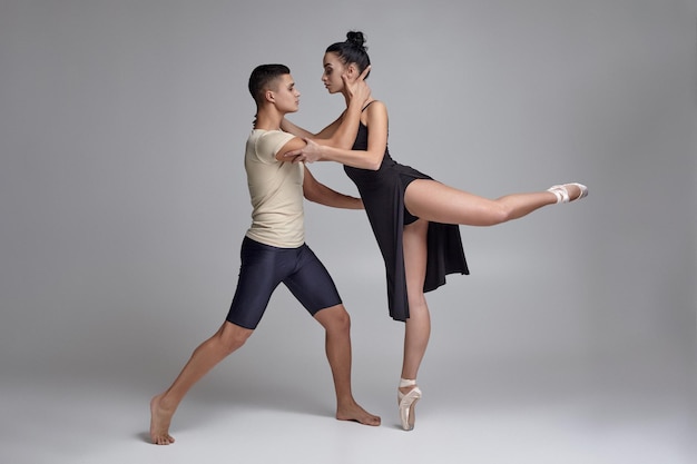 Two athletic modern ballet dancers are posing against a gray studio background