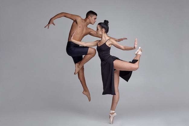 Two athletic modern ballet dancers are posing against a gray studio background