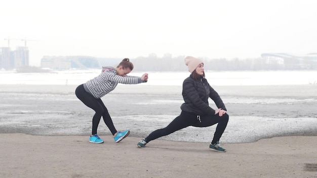 Two athletic women standing on the beach and warming up cold weather