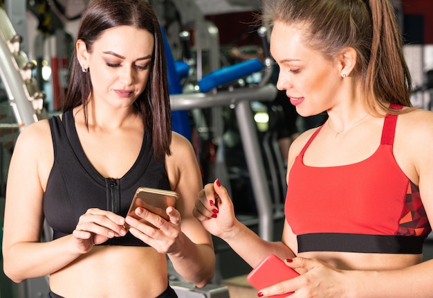 Two attractive fit women in gym with smart phone