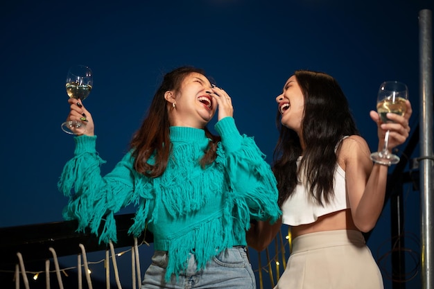 사진 두 명의 매력적인 재미있는 아시아 여성 친구들이 파티에서 춤을 추고  ⁇ 페인을 마시고 있습니다.