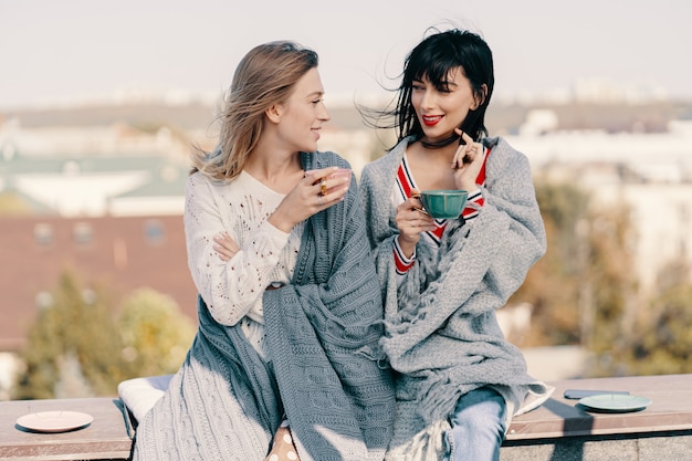 Two attractive girls enjoy a tea party on the rooftop overlooking the city