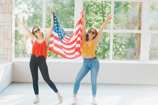 Две привлекательные молодые девушки в солнечных очках с американским флагом празднуют день независимости США