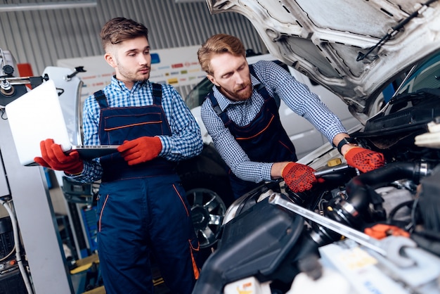 Two Auto Mechanics Work In Garage Over Broken Machine.