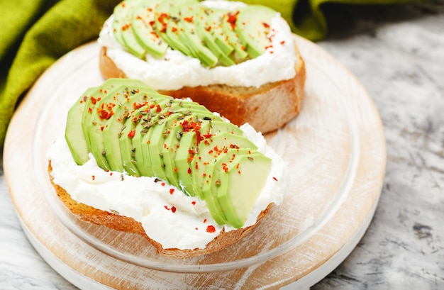 Two avocado toasts, avocado sandwich. Fresh avocado sliced on toast of wheat bread, cream cheese. Avocado sprinkled with chili, basil spices on a gray concrete background with place for text, top view