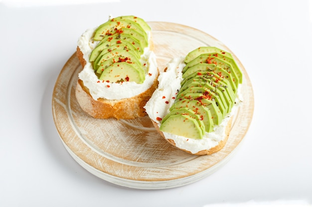 Two avocado toasts, avocado sandwich. Fresh avocado sliced on toast of wheat bread, cream cheese. Avocado sprinkled with chili, basil spices on a white background with place for text, top view.