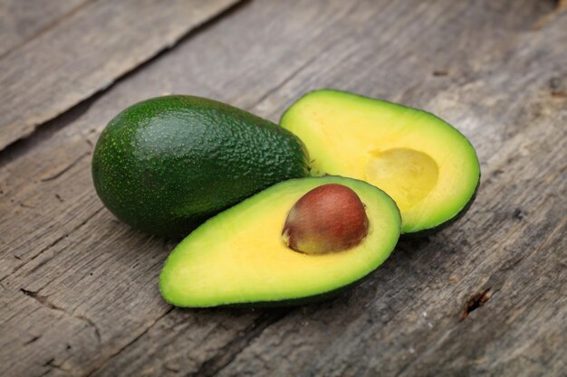 Two avocados one cut in two with seed on wooden surface