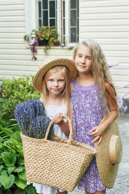 two baby girls in hats with a basket of lavender in a summer garden