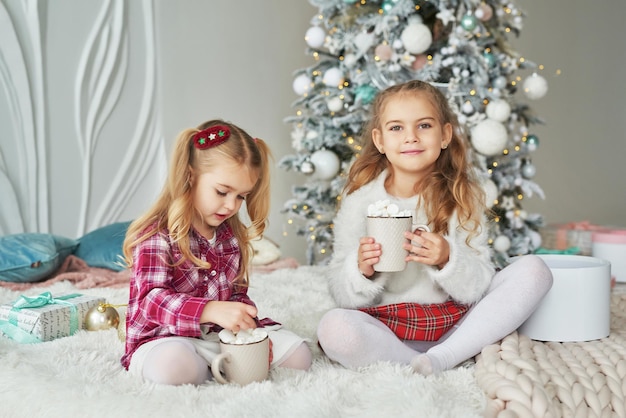Две сестры девочки на фоне рождественской елки. Счастливая семья. Концепция дружбы
