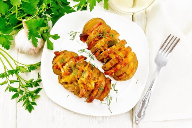 Two baked potatoes layered with smoked bacon and cheese in a plate on a napkin on wooden board background from above