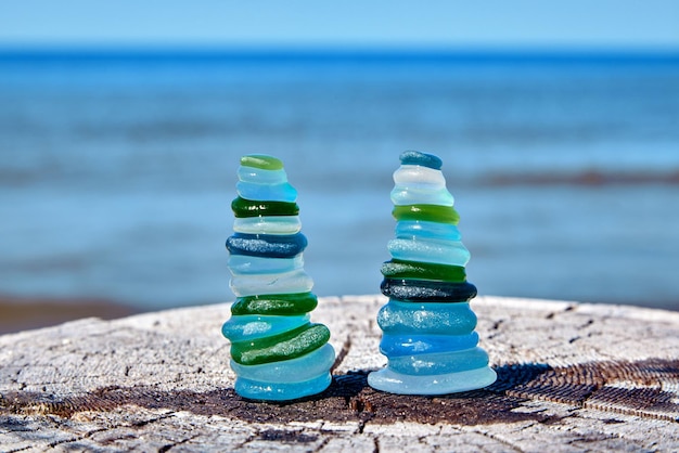 Two balanced pyramids of wet sea polished glass bottle shards on a weathered wooden surface against the sea