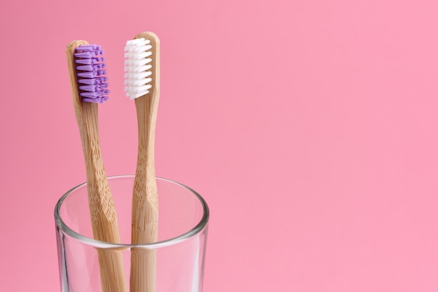 Two bamboo toothbrush close-up in glass on pink background. Eco friendly and zero waste concept photo.