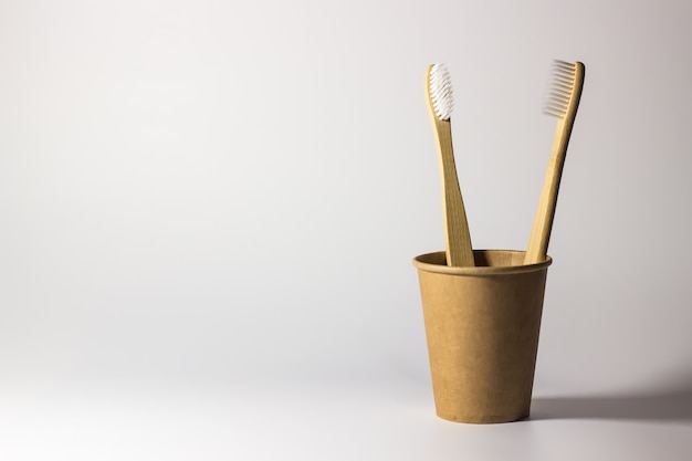 Photo two bamboo toothbrushes in a craft eco-friendlytwo bamboo toothbrushes in a craft eco-friendly glass on a white background glass on a white background