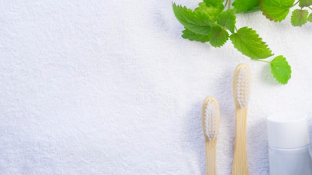 Two bamboo toothbrushes and mint leaves on a white towel