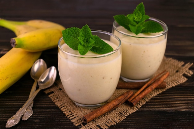 Two banana desserts with cinnamon in glasses on a dark wooden background