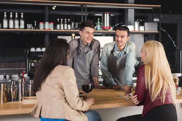 Two baristas chatting with guests at cafe counter. Men offering freshly brewed coffee to customers at modern bar interior, copy space. Occupation people and service concept