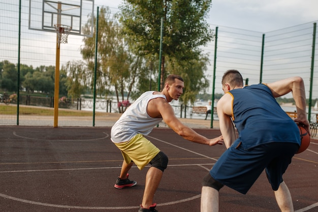 Two basketball players playing intense match on outdoor court.