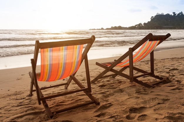 Foto due sedie a sdraio su una spiaggia con il sole che tramonta dietro di loro.