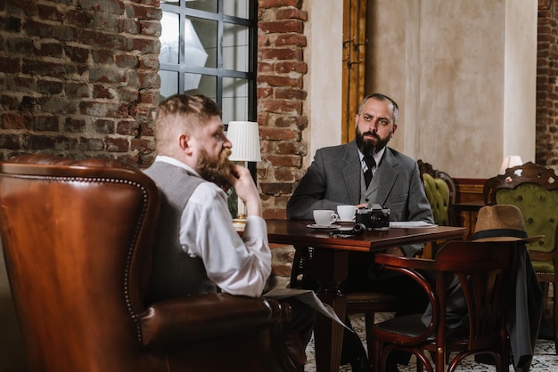 Two bearded men wearing old fashioned suits talking or discuss something in the restaurant