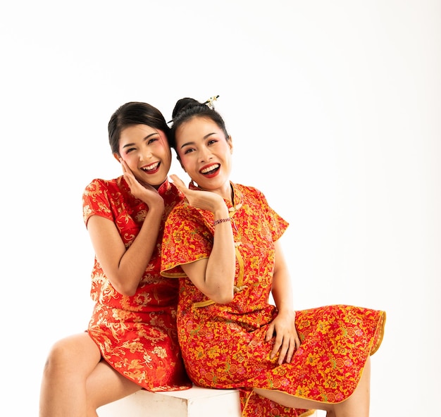 Two beautiful asian woman in red cheongsam sitting with hands at their chin and smiling showing thei